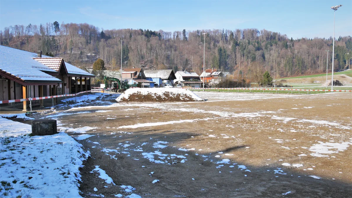 Man sieht eine Baustelle mit rot-weissen Abschrankungen, zwei Baggern und der Baugrube.